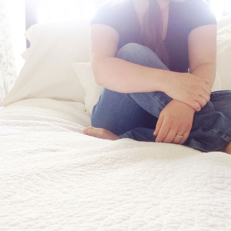 Woman sitting on bed with light flooding in behind her