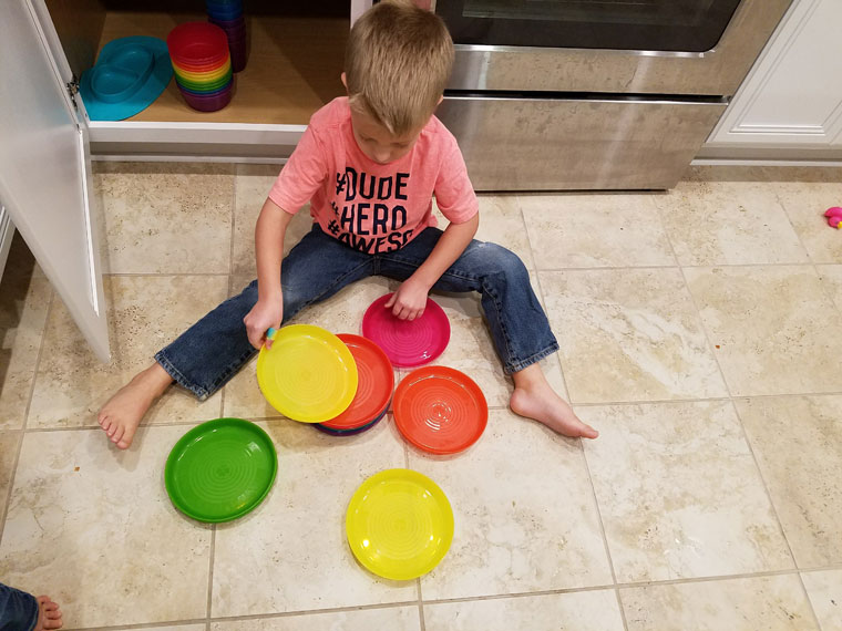Child sitting on floor with colorful plates dishes