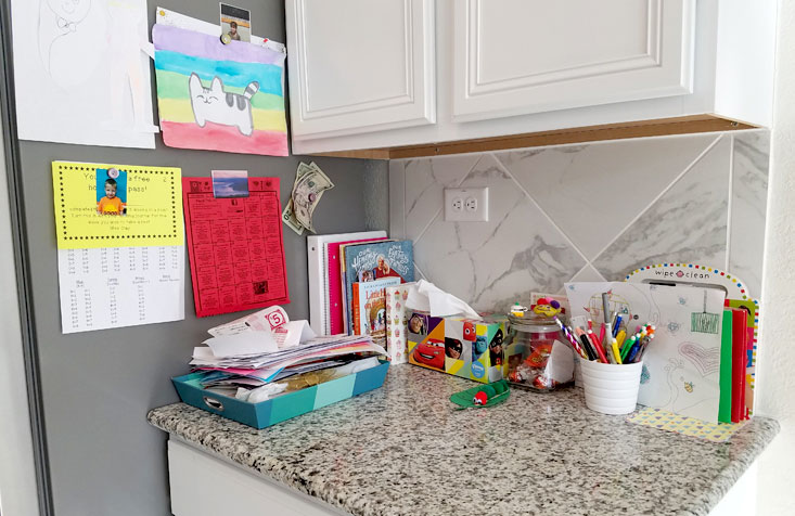 Kitchen command station overflowing with books, paperwork, and colorful writing utensils.