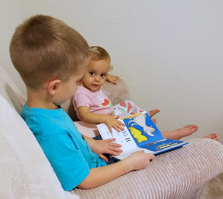 Boy reading a Dr. Suess book to his baby sister.