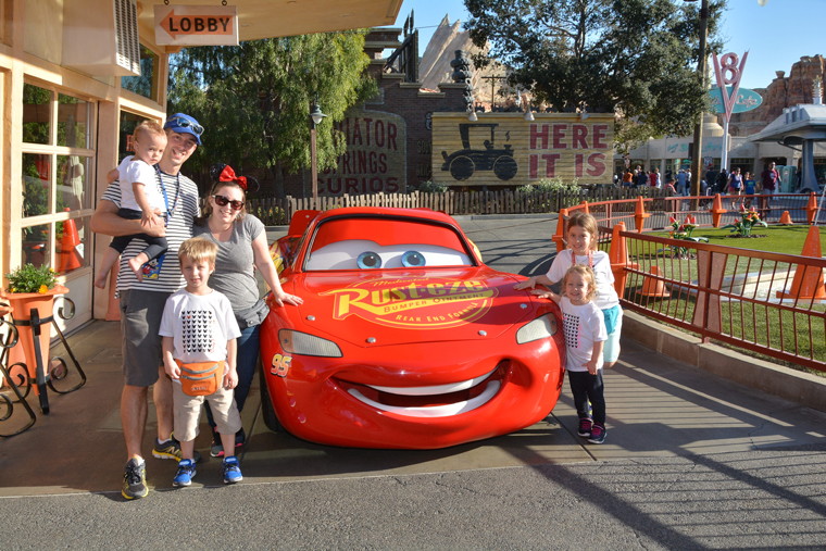 A family posing with Lightning McQueen after using one of the best Disneyland tips for families to get a free photo!