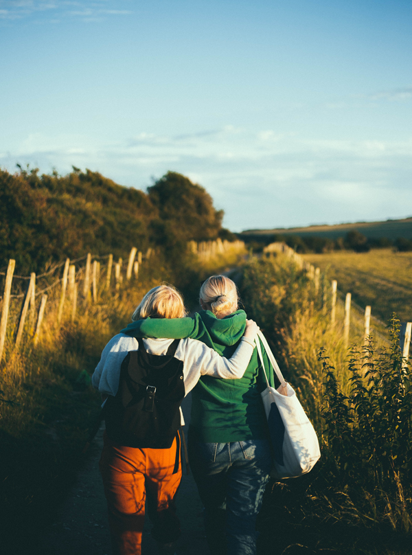 Friends walking through a field with their arms around each other.