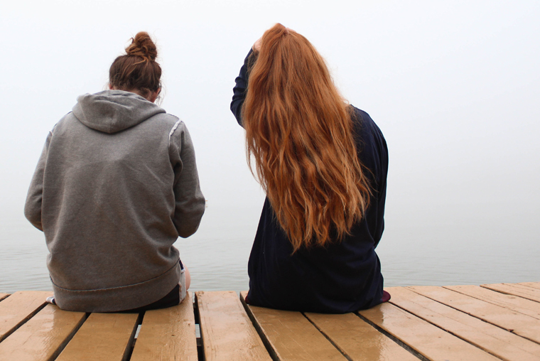 Two adult women friends sitting together on a dock.