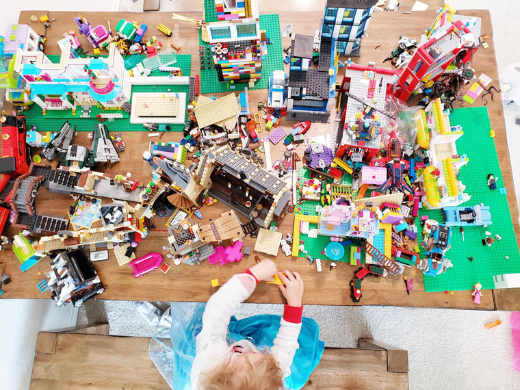 Child playing at a table strewn with Lego