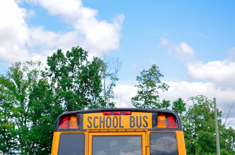Yellow school bus with green trees and blue sky