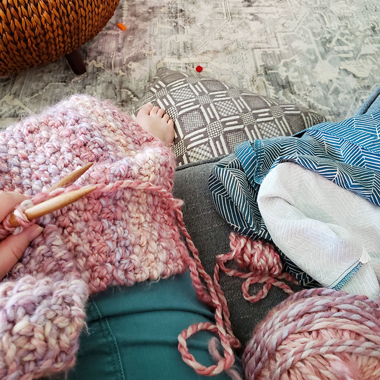 Half-knitted blanket sitting in a woman's lap.