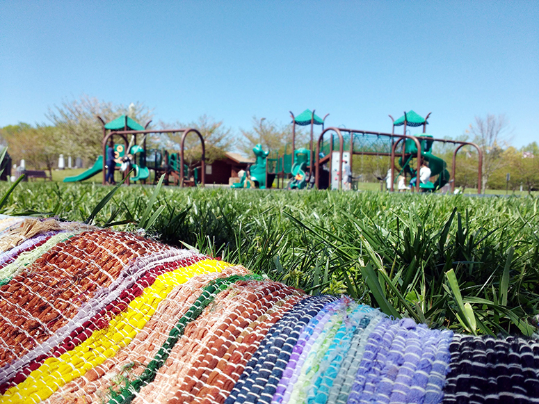 A colorful blanket spread in the grass by a playground.