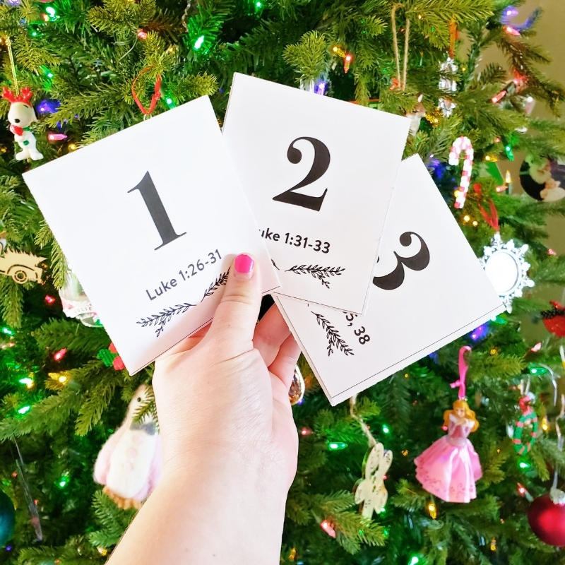 Hand holding a Christ-centered Christmas scripture advent in front of a Christmas tree